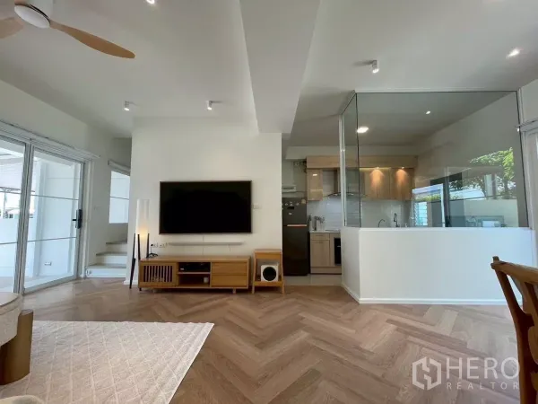 联排别墅 出租在Prawet, Bangkok - 客厅配壁挂电视，玻璃封闭式厨房，旁有推拉门。