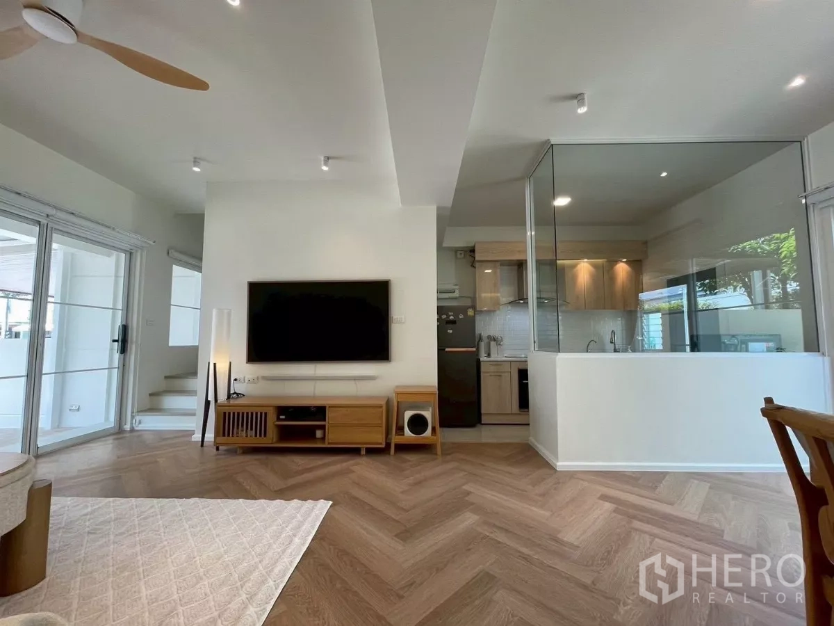 联排别墅 出租在Prawet, Bangkok - 客厅配壁挂电视，玻璃封闭式厨房，旁有推拉门。