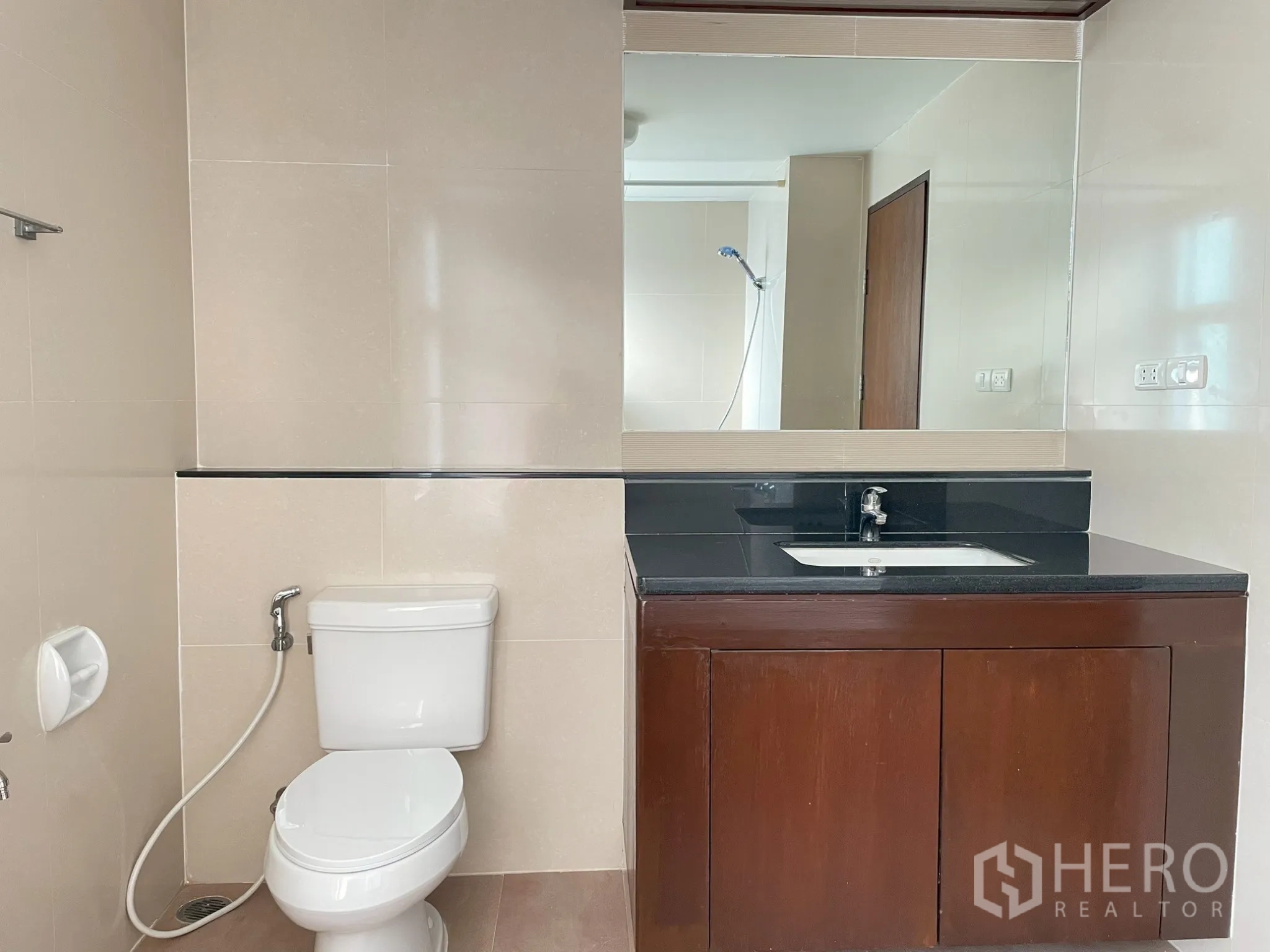 Apartment for rent in Khlong Toei, Bangkok - Bathroom with large mirror, vanity, and toilet.