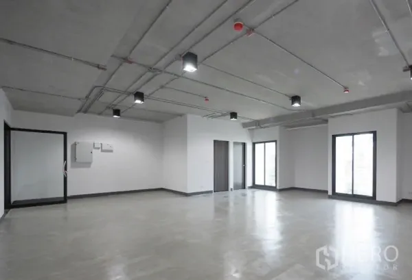Office Space for rent in Khlong Toei, Bangkok - Bright empty office interior featuring floor-to-ceiling windows, glass partition entry and utility panels beneath an industrial-style ceiling.