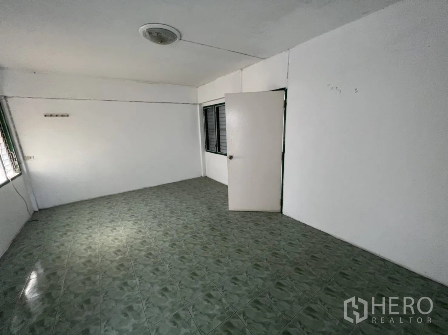 Townhouse for sale in Watthana, Bangkok - Spacious room with door and corner windows over green-tiled flooring.