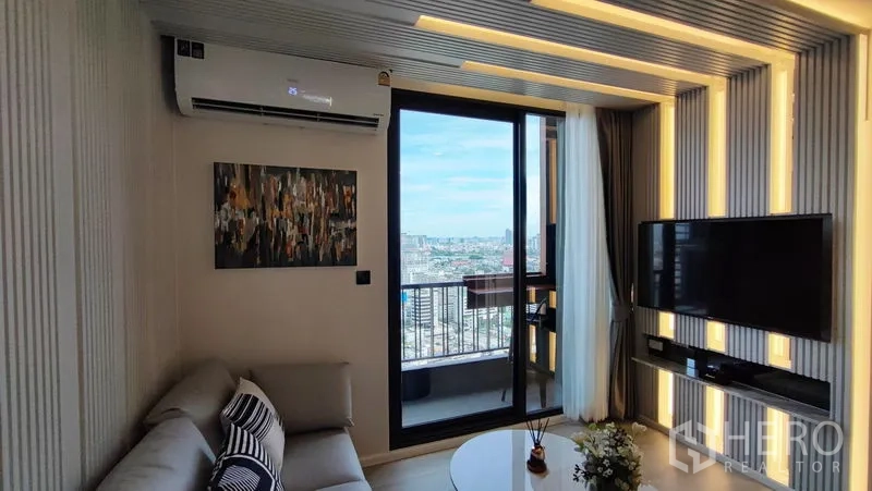 Condominium for rent in Bang Kho Laem, Bangkok - Lounge with wall-mounted TV and sliding doors to a balcony offering city and river views.
