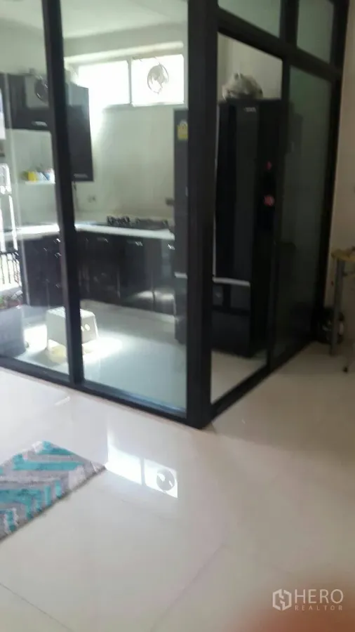 联排别墅 出租在Suan Luang, Bangkok - Noble Cube Suan Luang玻璃封闭式厨房，黑色橱柜、燃气炉和大冰箱。