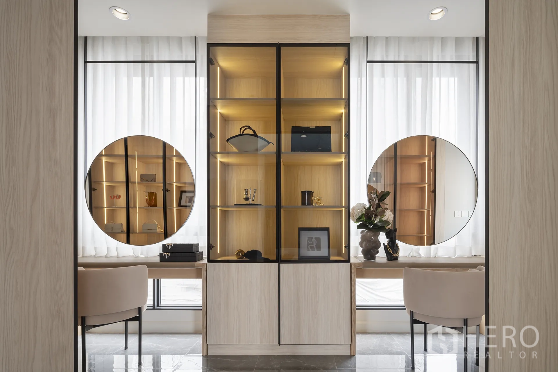 独栋房屋 for sale in Yan Nawa, Bangkok - 发光玻璃陈列柜，两侧为圆形镜面与内建书桌，软包椅与高挑纱帘窗相映成景。