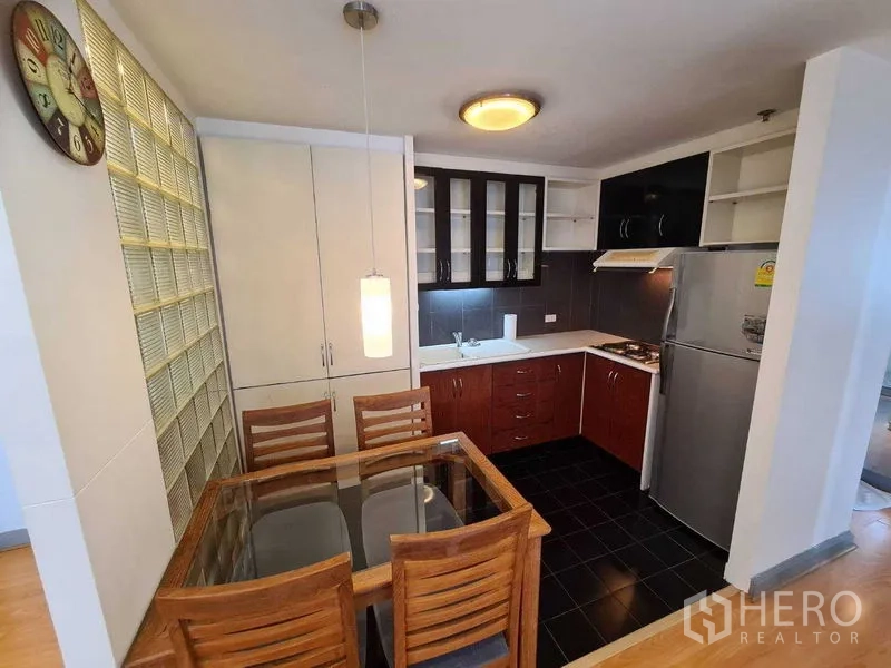 Condominium for rent in Ratchathewi, Bangkok - Compact L-shaped kitchen with cabinets, pendant light and dining table.
