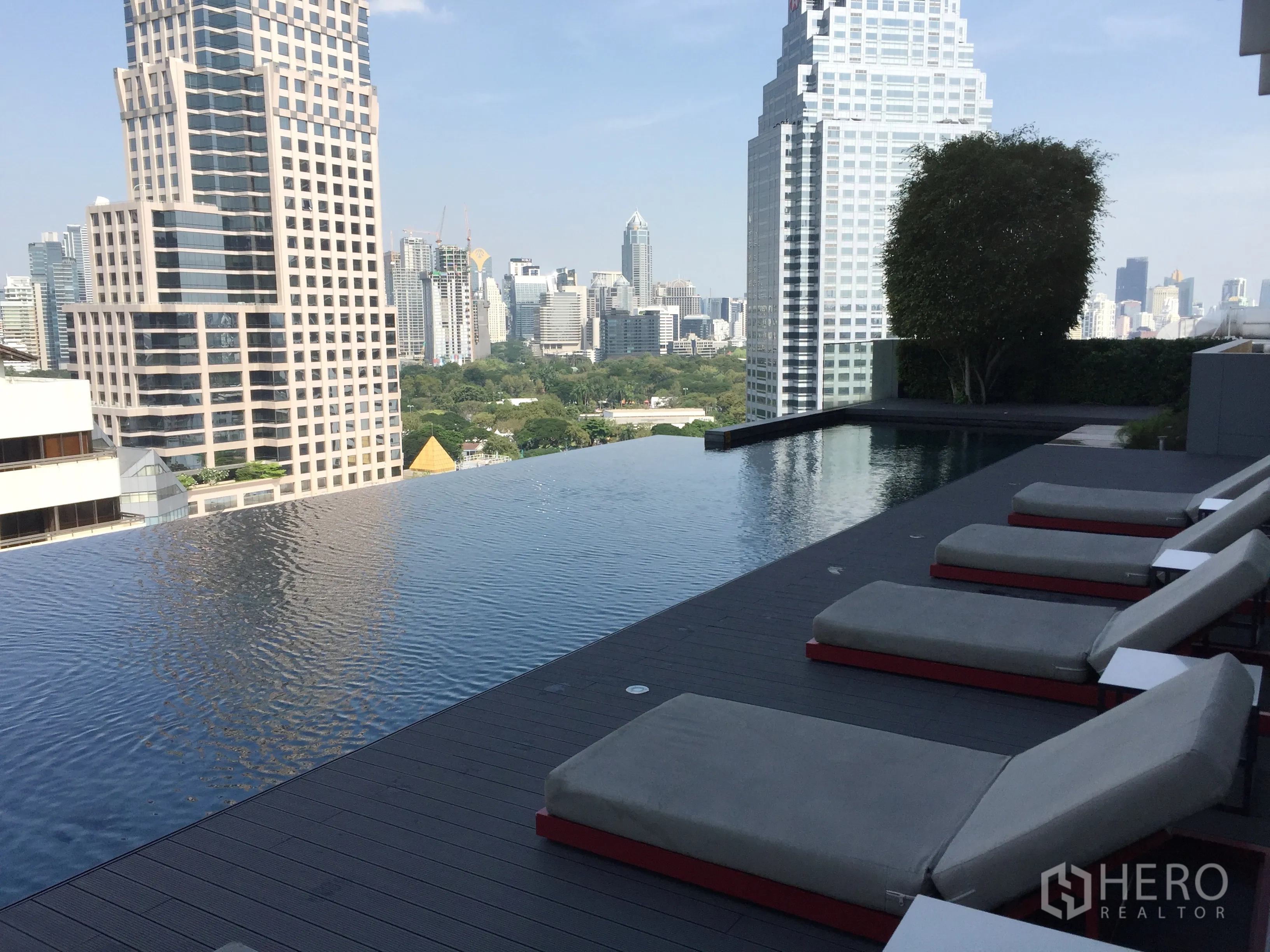 公寓 出租在Bang Rak, Bangkok - 屋顶无边际泳池，躺椅与城市天际线景观，可望伦披尼公园。