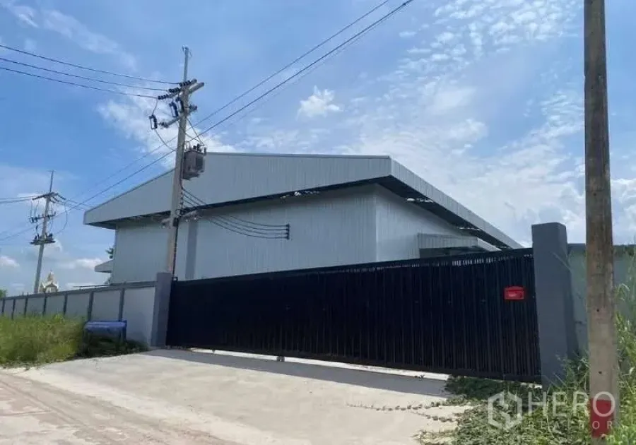 Warehouse for sale in Ban Bueng, Chon Buri - Modern metal-clad warehouse exterior with tall black sliding gate, perimeter wall, and power lines in Ban Bueng, Chon Buri.