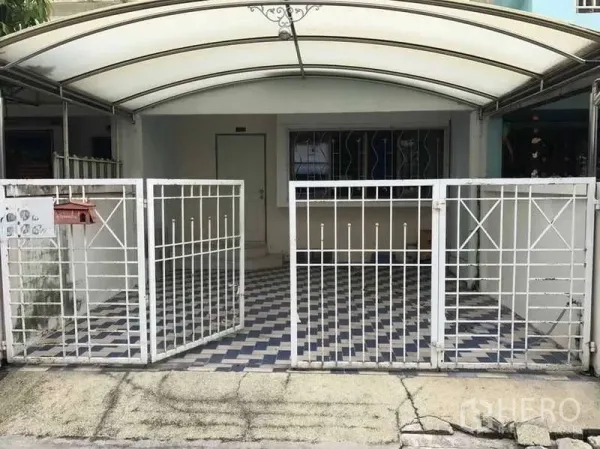 联排别墅 出租在Suan Luang, Bangkok - 联排别墅正面，白色金属大门，带顶车棚与棋盘格地面。