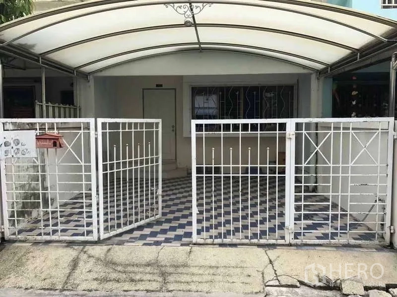 ทาวน์เฮาส์ ให้เช่าในSuan Luang, Bangkok - ด้านหน้าทาวน์เฮ้าส์มีกันสาด โรงจอดรถ และรั้วเหล็กสีขาวพื้นลายตาราง