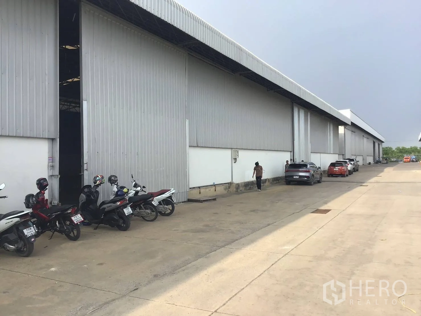 Warehouse for rent in Lat Krabang, Bangkok - Exterior side of warehouse with large sliding door and parking along a wide access road.