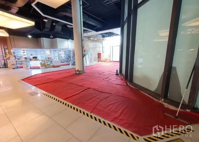Retail Space for rent in Khlong Toei, Bangkok - Open-plan shop space with glass walls, a structural pillar, red floor covering and a bright tiled concourse in a mall setting.