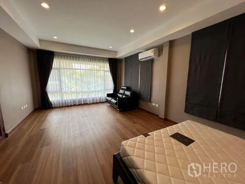 Detached House for sale in Mueang Pathum Thani, Pathum Thani - Spacious bedroom with wood flooring, full-height window, air conditioner and lounge chair