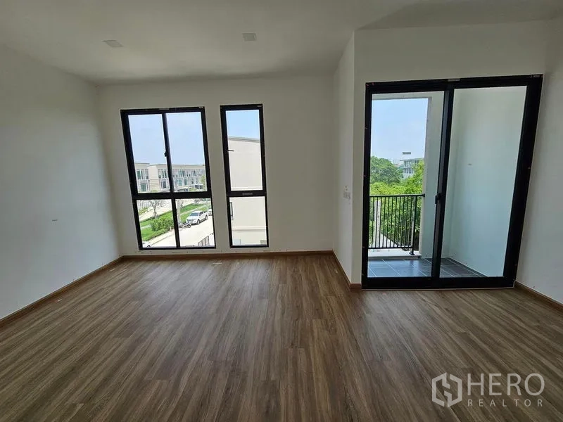 联排别墅 出租在Bang Kapi, Bangkok - 阳光卧室，木质地板，高窗与通向小阳台的推拉门，景观绿意。