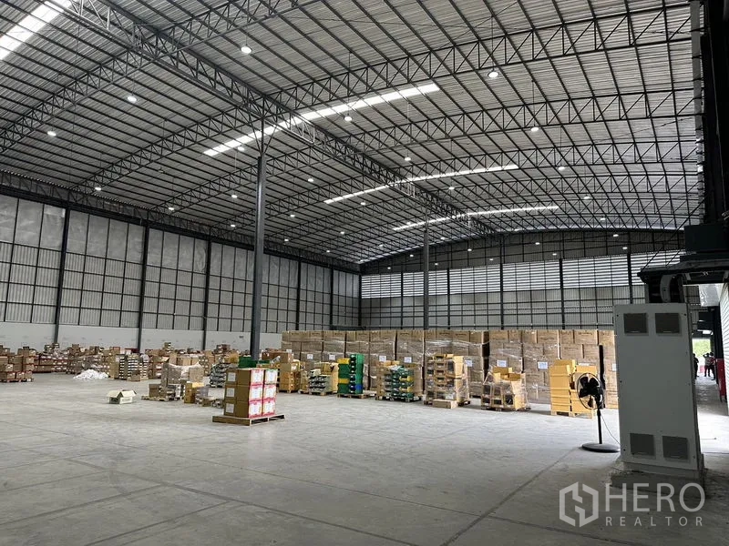 Warehouse for rent in Lat Krabang, Bangkok - Expansive warehouse hall with tall ceilings, skylights and stacked boxes ready for distribution.