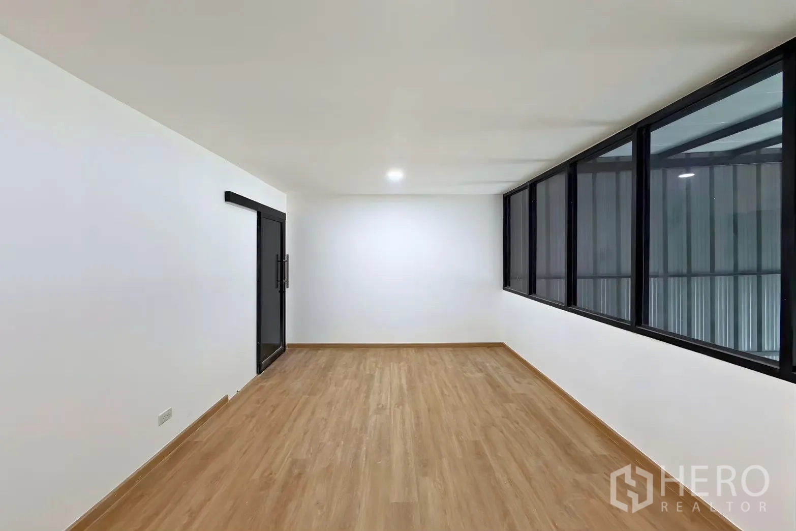 Warehouse for rent in Suan Luang, Bangkok - Empty office room with wood-look flooring, sliding door, and long interior window.
