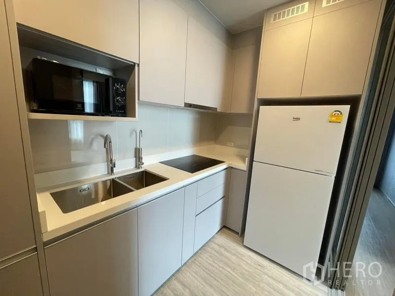 Condominium for rent in Samut Prakan - Bright galley kitchen with double sinks, cooktop, microwave and refrigerator.
