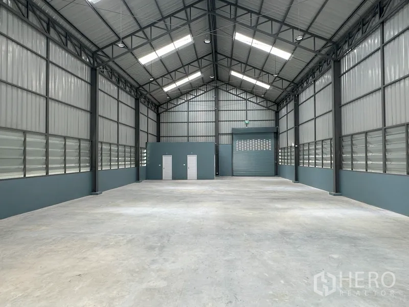 Factory for rent in Khlong Luang, Pathum Thani - Warehouse interior facing roller door and service rooms, bright from roof lights.