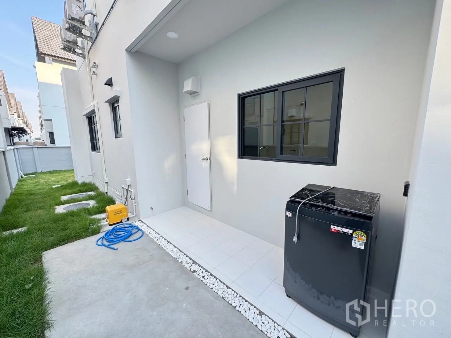 Detached House for rent in Bang Phli, Samut Prakan - Outdoor service yard with washing machine, tiled patio, and grass path along the wall.