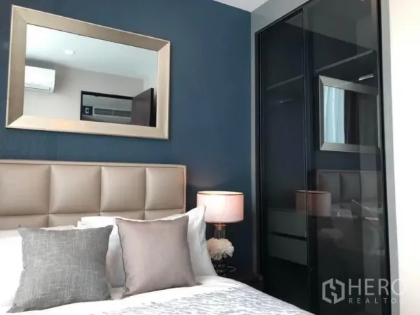 Condominium for rent or sale in Ratchathewi, Bangkok - Bright bedroom featuring padded headboard, pillows, bedside lamp, and a glass-door wardrobe.