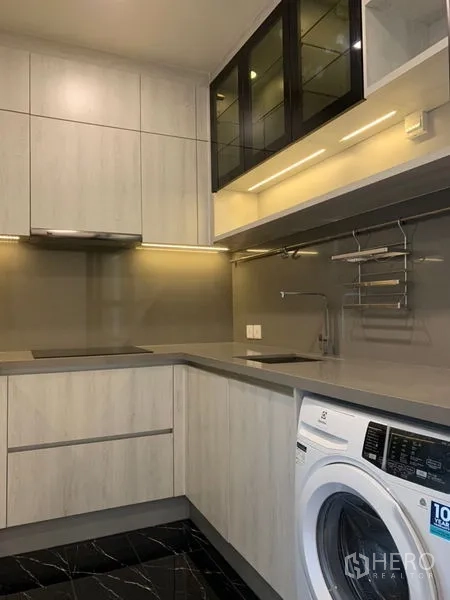 Condominium for sale in Khlong Toei, Bangkok - U-shaped kitchen with induction hob, ample cabinetry and front-load washing machine.