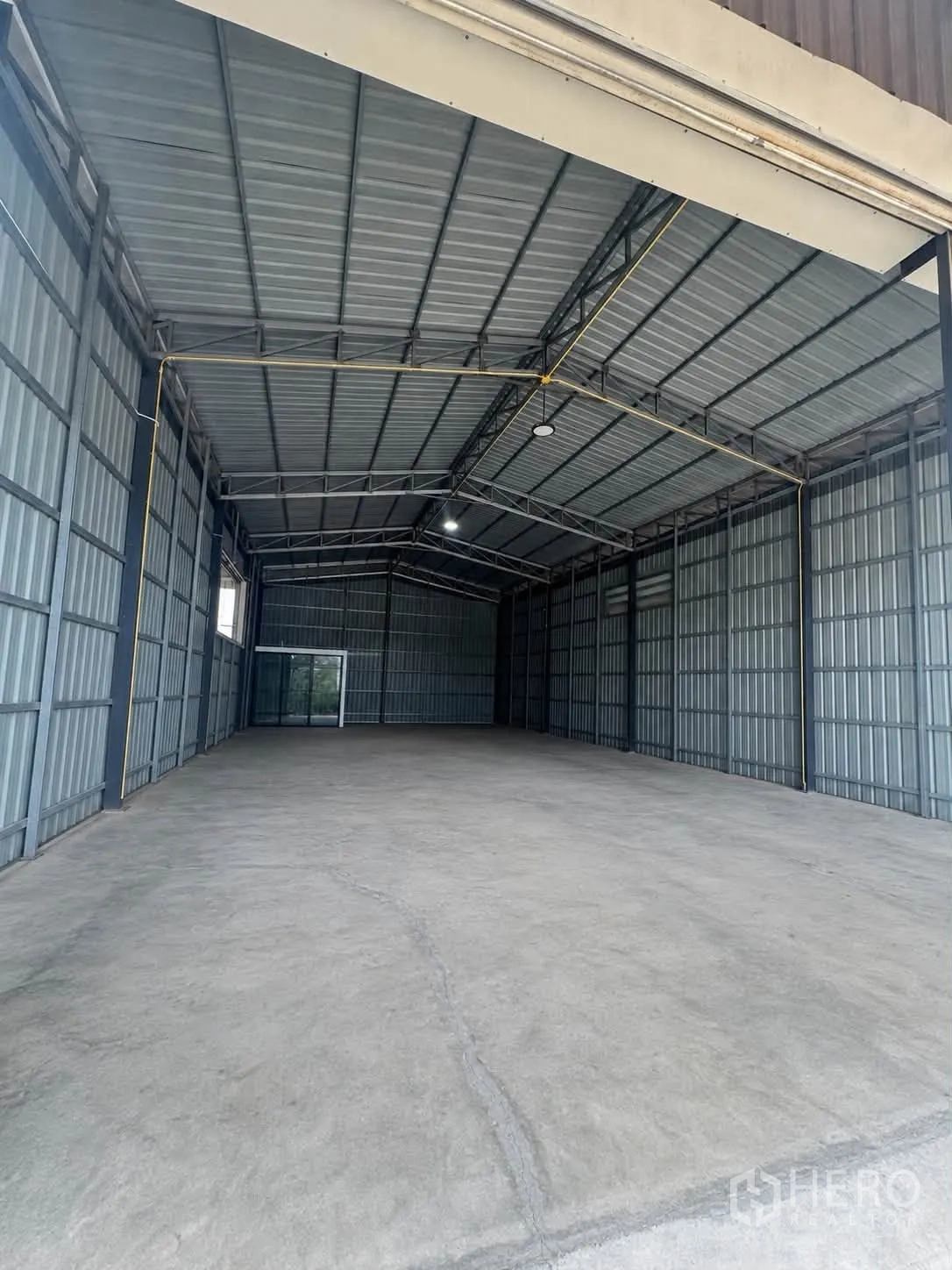 Warehouse for rent in Bang Kruai, Nonthaburi - Interior of warehouse with concrete floor, steel frame, metal cladding, ceiling lights, and a rear glass door.