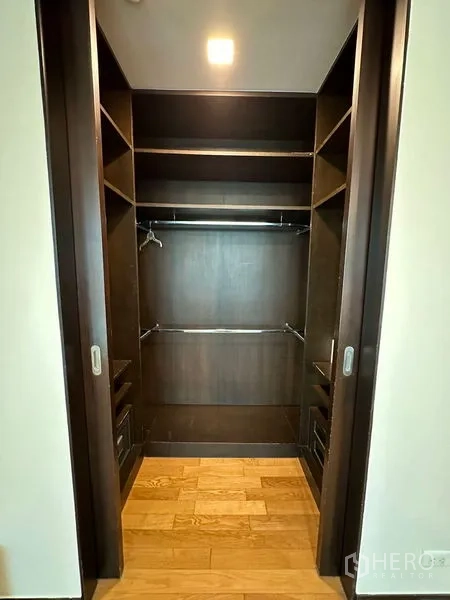 Condominium for rent in Yan Nawa, Bangkok - Walk-in closet with dark wood shelving and hanging rails.