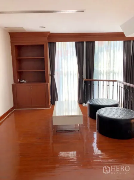 Townhouse for rent in Khlong Toei, Bangkok - Mezzanine lounge with built-in shelving, floor-to-ceiling curtains and glossy wood floors.