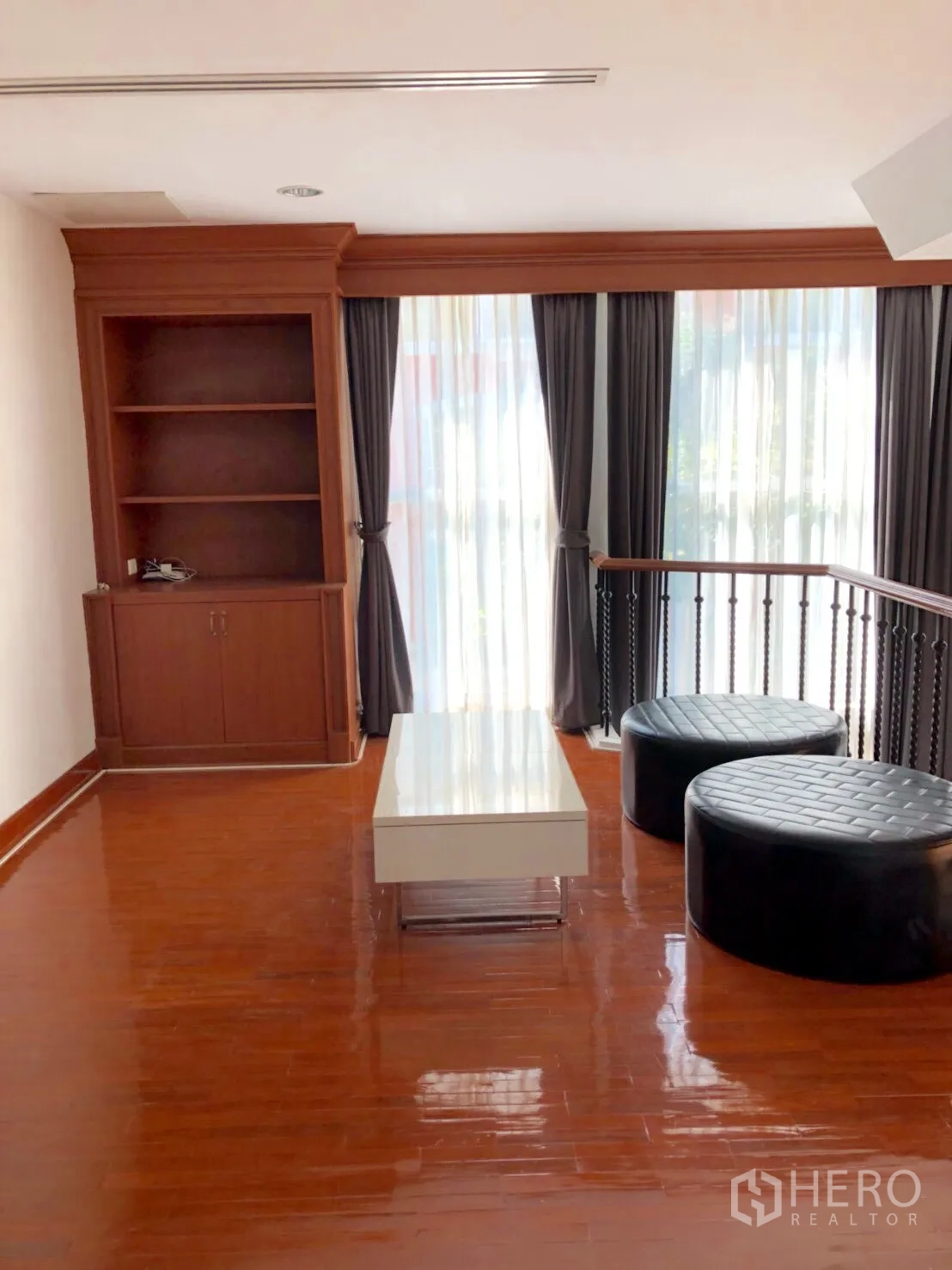 Townhouse for rent in Khlong Toei, Bangkok - Mezzanine lounge with built-in shelving, floor-to-ceiling curtains and glossy wood floors.