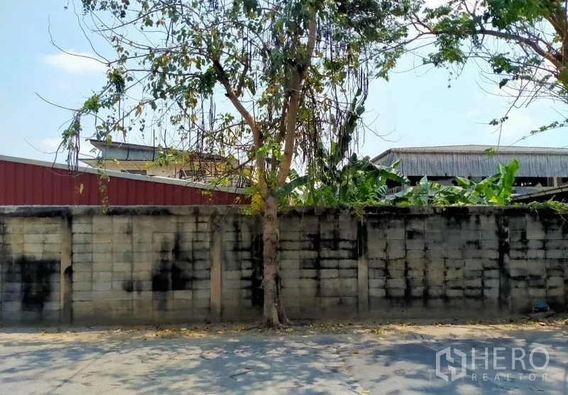 Warehouse for sale in Mueang Nonthaburi, Nonthaburi - Street-side boundary wall with trees screening the property.