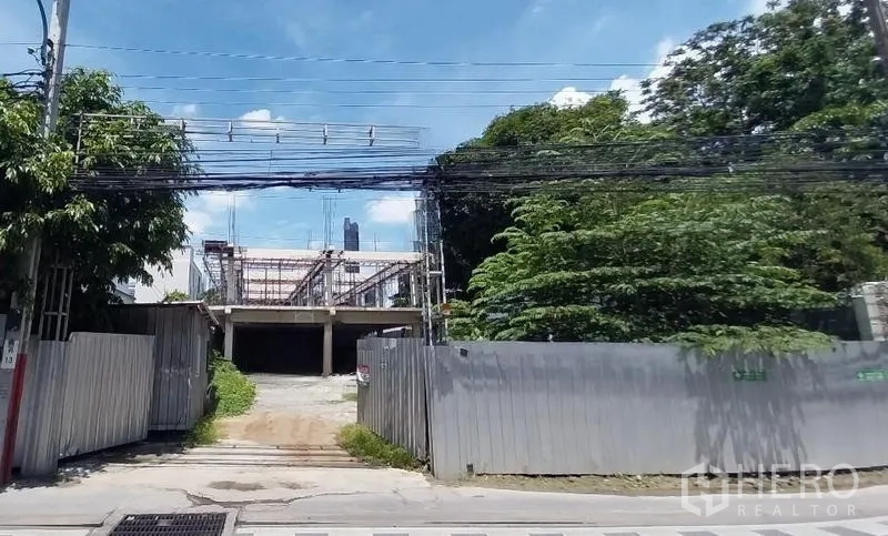 Land for rent in Khlong Toei, Bangkok - Front view of fenced development site with wide gate, partial structure, and overhead utility lines near Sukhumvit Road.