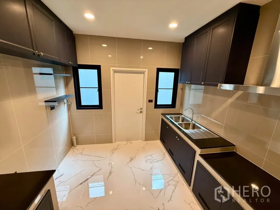 Detached House for rent in Don Mueang, Bangkok - Modern separate kitchen with dark cabinetry, double sink, and tiled walls.
