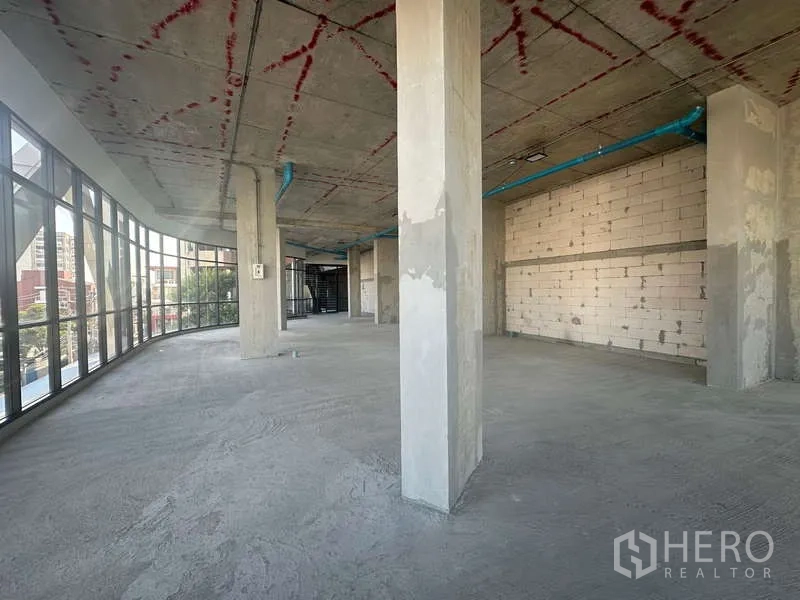 零售空间 出租在Phra Khanong, Bangkok - 宽阔零售楼层，弧形窗带、立柱与带红记号的混凝土顶。