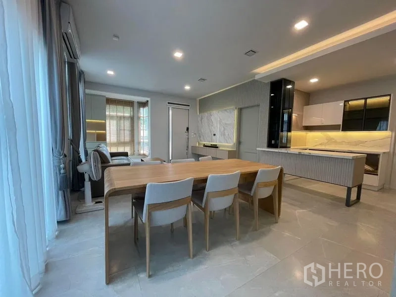 บ้าน ให้เช่าในPrawet, Bangkok - โถงนั่งเล่น–ทานอาหารแบบเปิดโล่ง โต๊ะไม้ ผ้าม่านโปร่ง และฉากหลังเป็นครัวทันสมัย