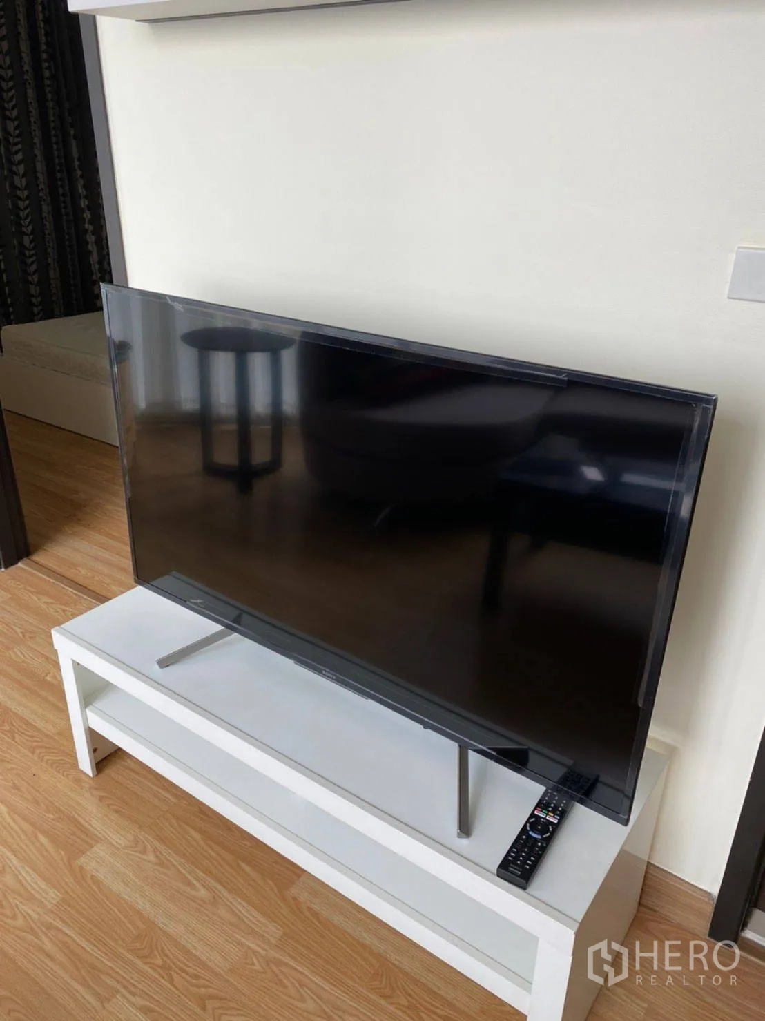 Condominium for rent in Watthana, Bangkok - Flat-screen TV on a white media console with remote on wood flooring.