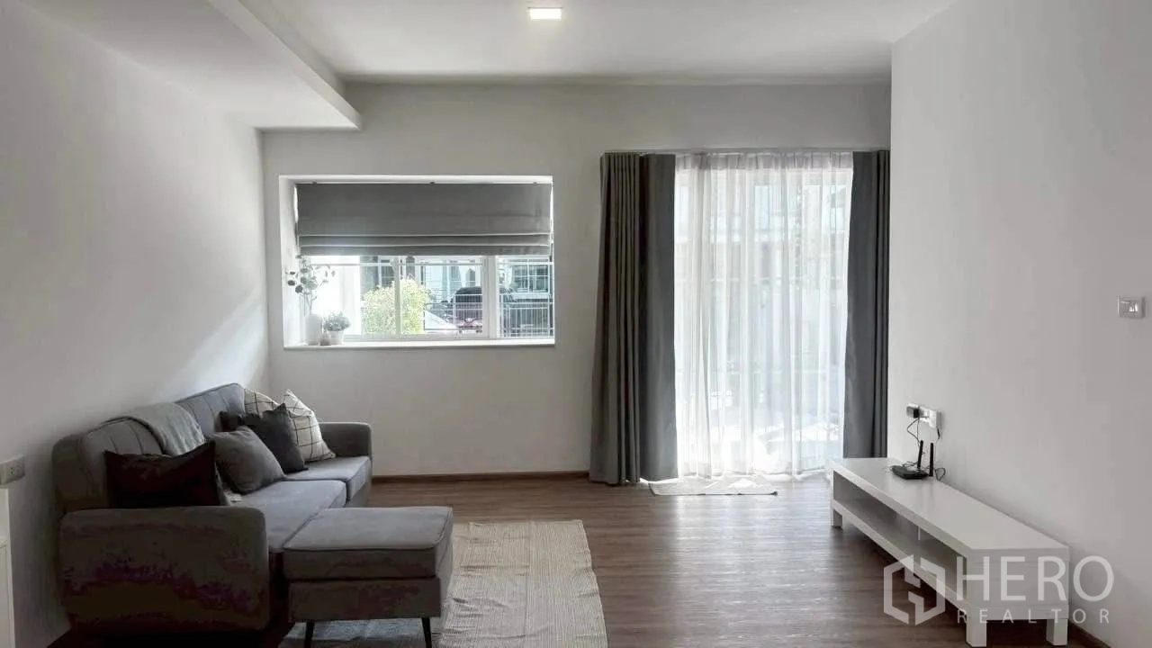 Townhouse for rent in Prawet, Bangkok - Bright living room with L-shaped sofa, TV console and sliding glass doors to the terrace.