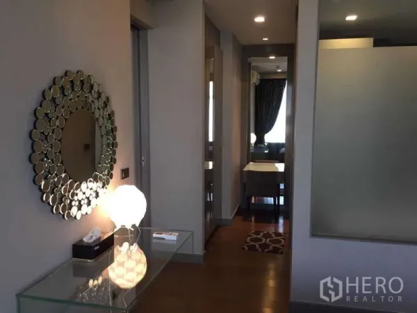 Condominium for rent in Bang Rak, Bangkok - Entrance hallway with decorative circular mirror, glass console and wood flooring.
