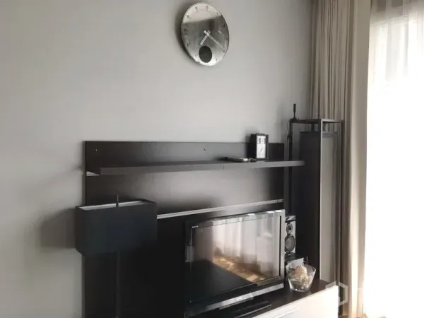 คอนโด ให้เช่าในKhlong Toei, Bangkok - มุมนั่งเล่นสว่างด้วยทีวีคอนโซล ชั้นวางลอย โคมไฟตั้งพื้น นาฬิกาติดผนัง และผ้าม่านโปร่ง