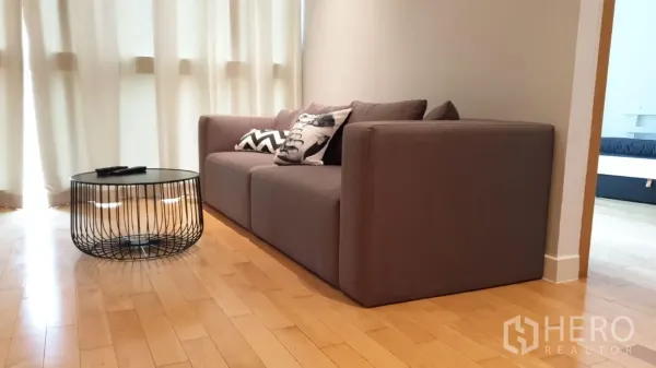 Condominium for rent or sale in Khlong Toei, Bangkok - Cozy gray sofa with patterned cushions beside a round wire coffee table near the window.