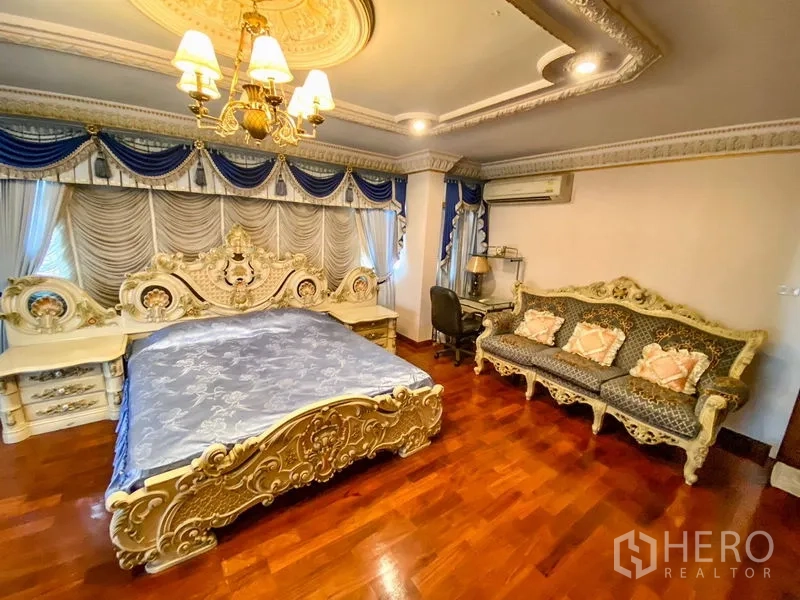 独立式住宅 出租或出售在Bang Khen, Bangkok - 宽大卧室，蓝色窗帘、雕花大床与木地板沙发。