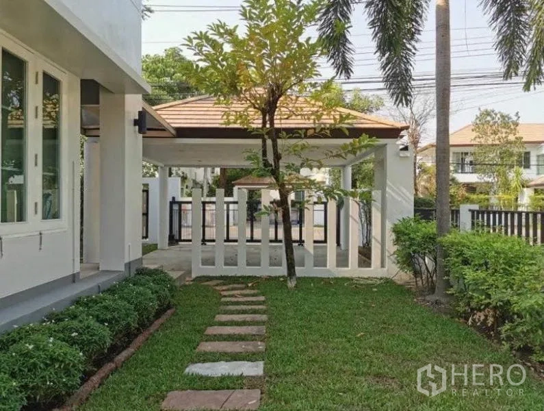 Detached House for rent in Bang Kapi, Bangkok - Front garden with stepping stones, landscaped shrubs and a covered carport inside a gated area.