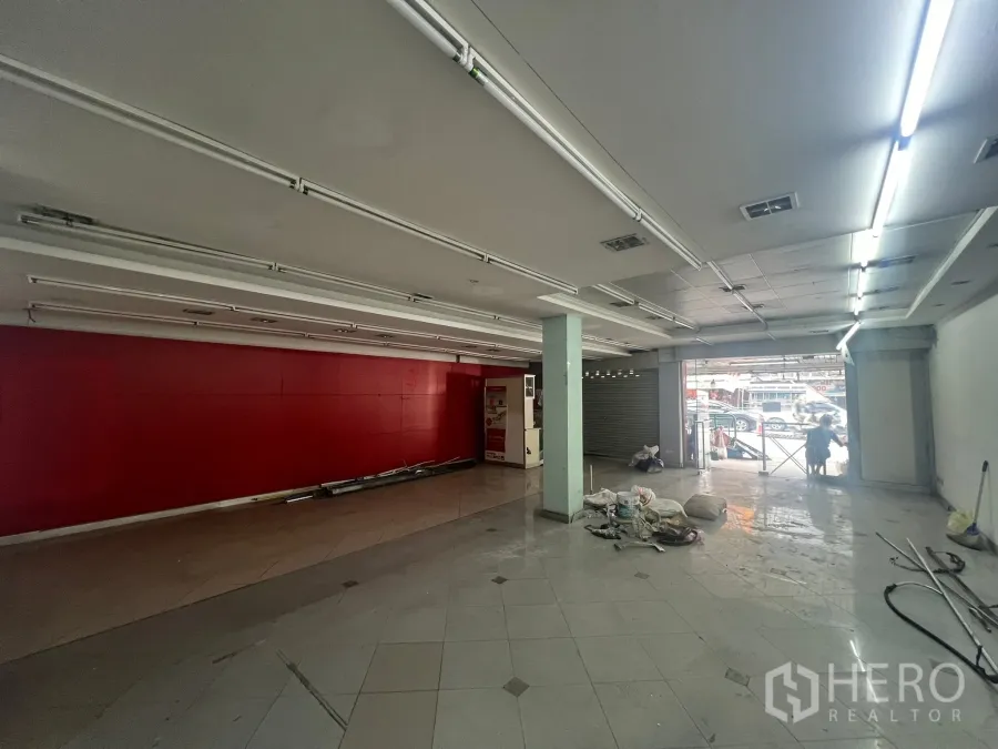 店屋 出租在Watthana, Bangkok - 临街一层商铺大厅，红色特色墙、瓷砖地面、日光灯与卷闸门门面。