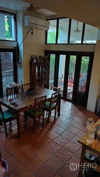 Detached House for sale in Suan Luang, Bangkok - Dining area with terracotta tiles, wooden table and glass doors opening to a garden terrace.