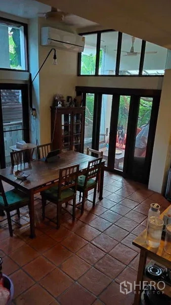 Detached House for sale in Suan Luang, Bangkok - Dining area with terracotta tiles, wooden table and glass doors opening to a garden terrace.