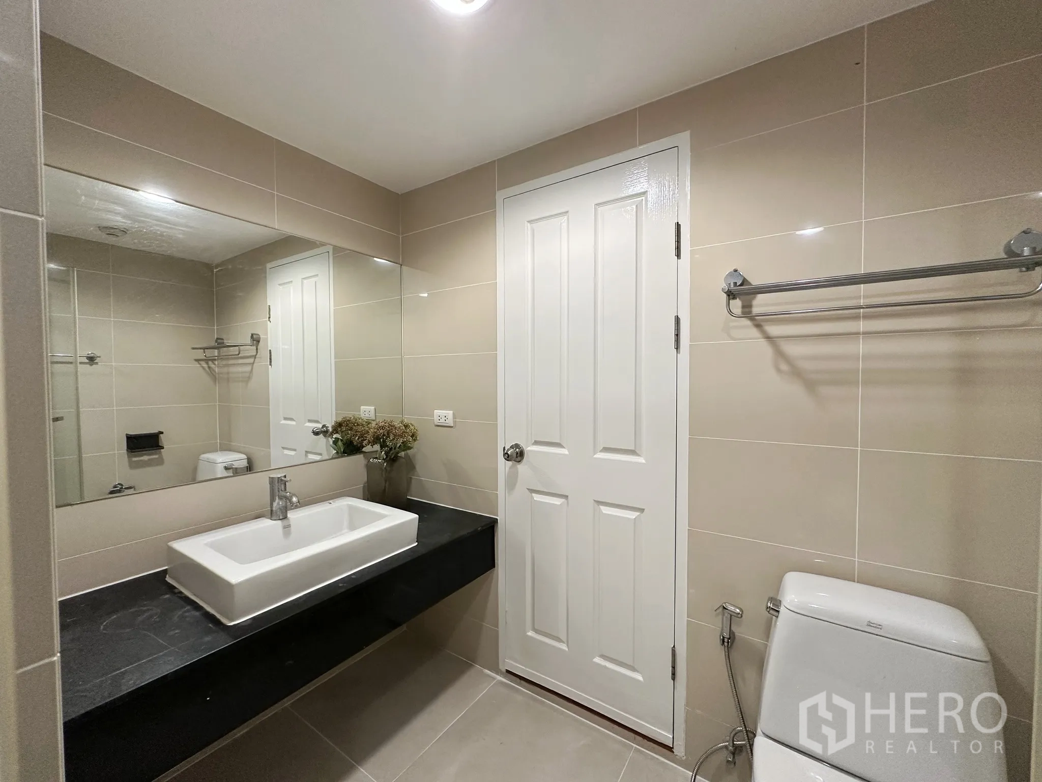 คอนโด for sale in Huai Khwang, Bangkok - ห้องน้ำโมเดิร์นมีกระจกบานใหญ่ อ่างล้างหน้าทรงสี่เหลี่ยมบนท็อปหินสีดำ และโถสุขภัณฑ์.