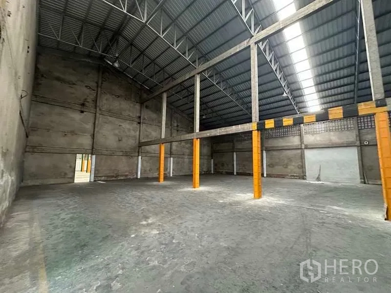 货栈 出租在Mueang Pathum Thani, Pathum Thani - 开阔地面与高挑屋顶，立柱涂有安全警示色。