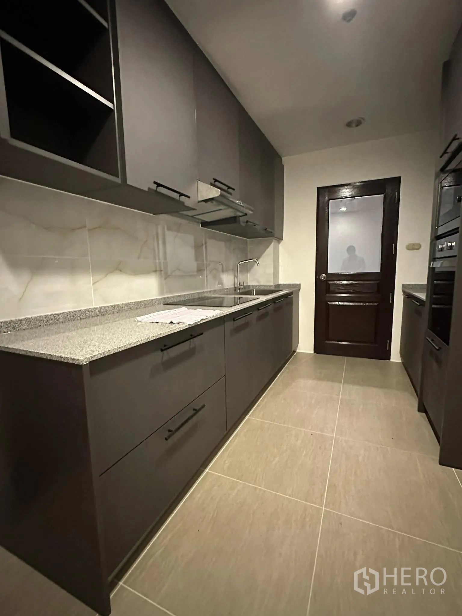 公寓 for rent in Pathum Wan, Bangkok - 走廊式厨房，深色橱柜与石材台面，配实木门。