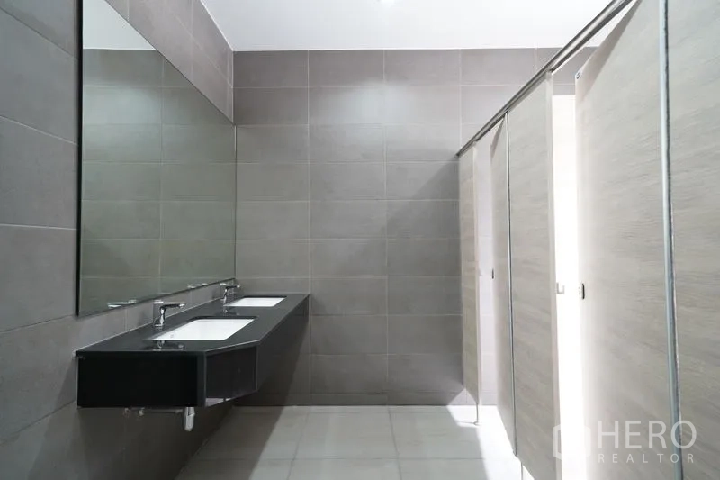 Warehouse for rent in Khlong Luang, Pathum Thani - Tiled restroom with long mirror, twin sinks, and private stalls.
