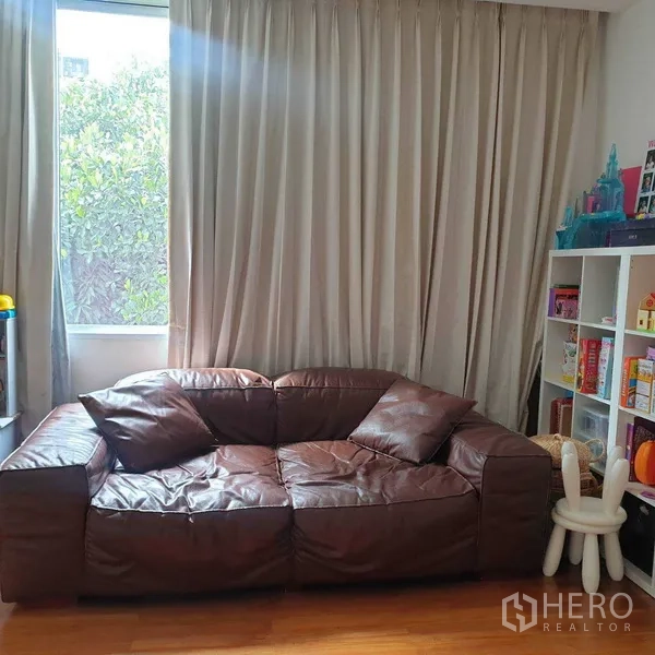 Detached House for rent in Watthana, Bangkok - Cozy family room with brown leather sofa, large window and shelving, curtains drawn.