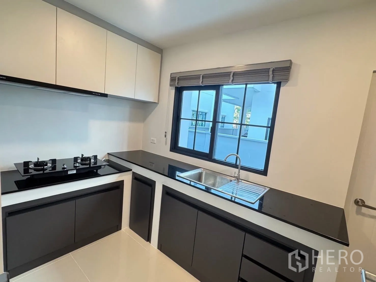 Detached House for rent in Bang Phli, Samut Prakan - Modern kitchen with black stone countertops, gas cooktop, and sink beneath a window.