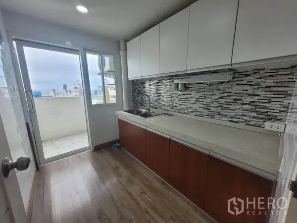 公寓 出租在Watthana, Bangkok - 独立厨房，长台面与马赛克墙面，门通向可眺望天际线的生活阳台。